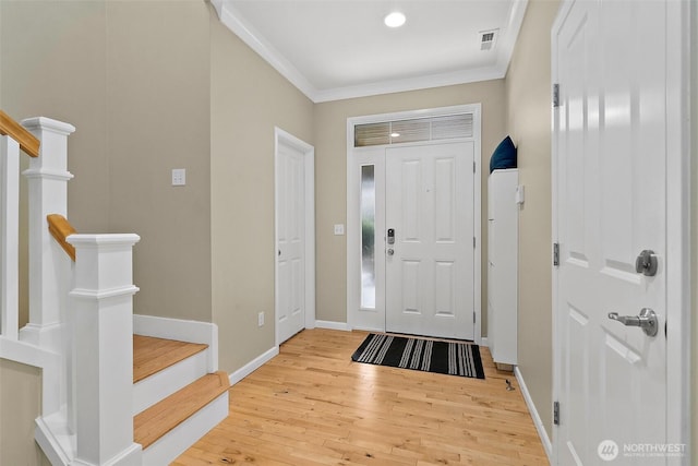 entryway with visible vents, baseboards, light wood-style floors, ornamental molding, and stairway