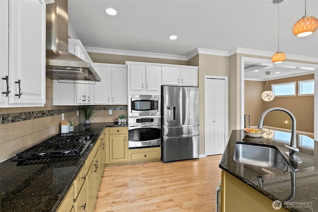 kitchen with wall chimney range hood, crown molding, stainless steel appliances, and a sink