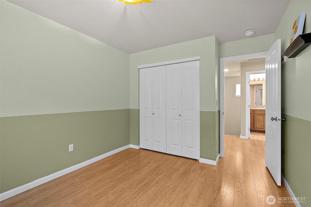 unfurnished bedroom featuring light wood-style flooring, baseboards, and a closet