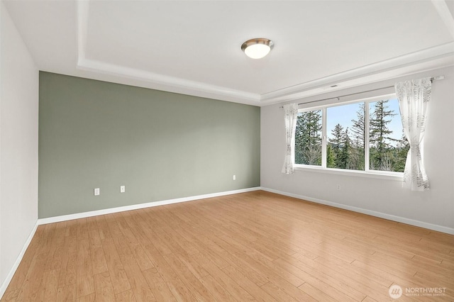 empty room featuring light wood-style flooring, baseboards, and a raised ceiling