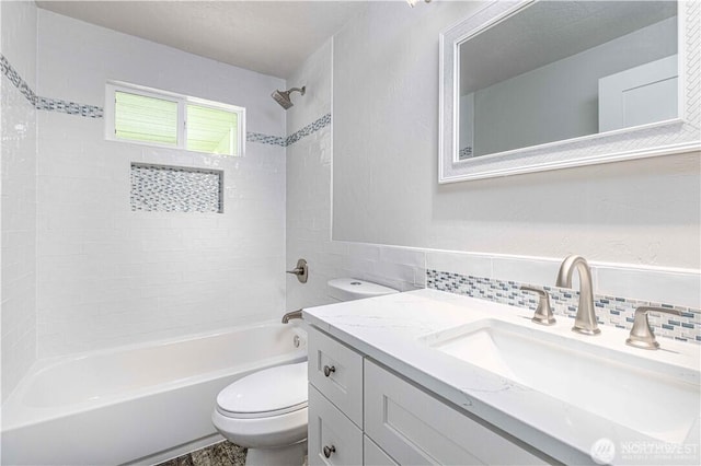 full bathroom with tile walls, tub / shower combination, vanity, and toilet