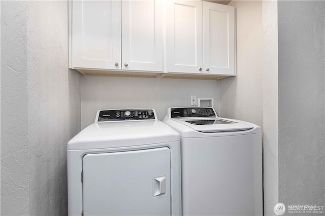 washroom with a textured wall, washing machine and clothes dryer, and cabinet space