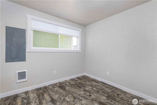 empty room featuring dark wood-style flooring, electric panel, visible vents, and baseboards