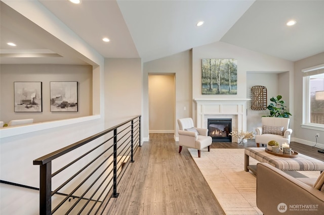 interior space with recessed lighting, a glass covered fireplace, vaulted ceiling, and wood finished floors