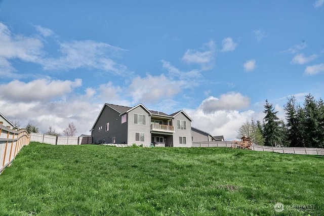 rear view of house with a fenced backyard, a lawn, and a balcony