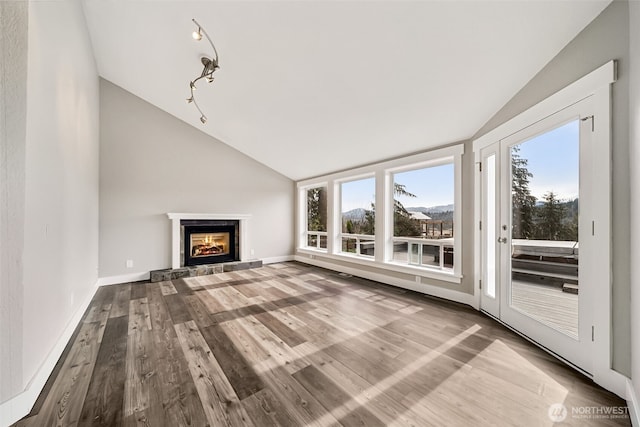 unfurnished living room featuring a glass covered fireplace, baseboards, wood finished floors, and vaulted ceiling