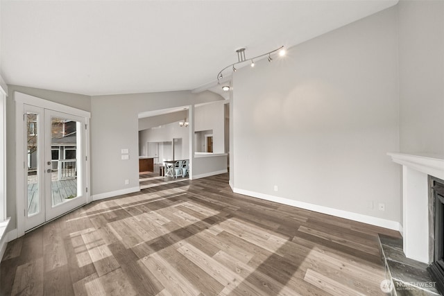 unfurnished living room with a fireplace with raised hearth, wood finished floors, french doors, baseboards, and lofted ceiling