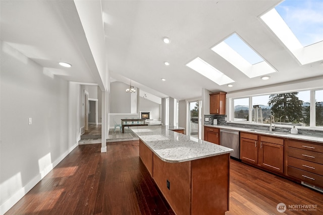 kitchen with light stone counters, a kitchen island, stainless steel dishwasher, brown cabinetry, and vaulted ceiling