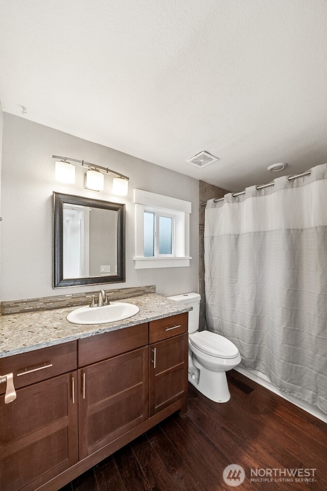 full bath featuring visible vents, toilet, a shower with curtain, wood finished floors, and vanity