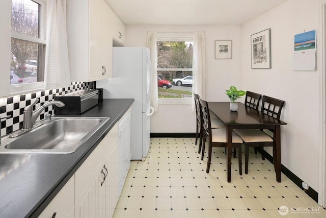 kitchen featuring white dishwasher, a sink, white cabinets, light floors, and dark countertops