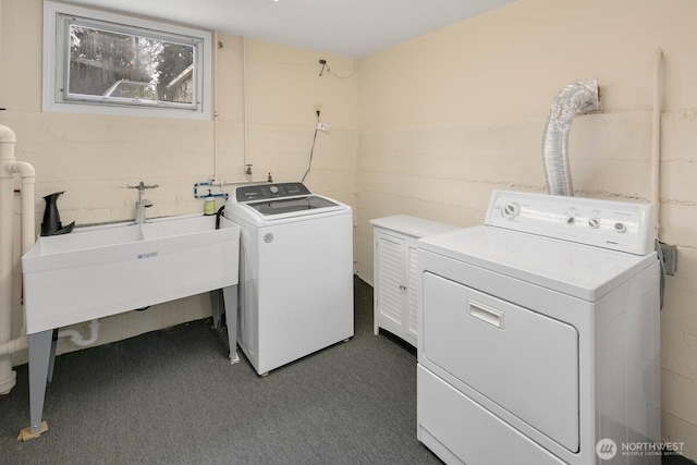 clothes washing area with concrete block wall, dark carpet, washer and clothes dryer, and a sink