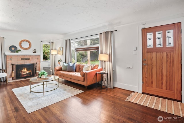 living area with dark wood-style floors, a textured ceiling, a brick fireplace, and baseboards