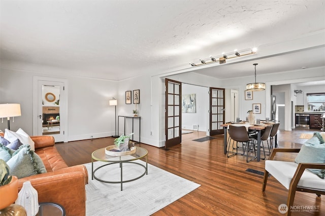 living room featuring a textured ceiling, wood finished floors, visible vents, baseboards, and french doors