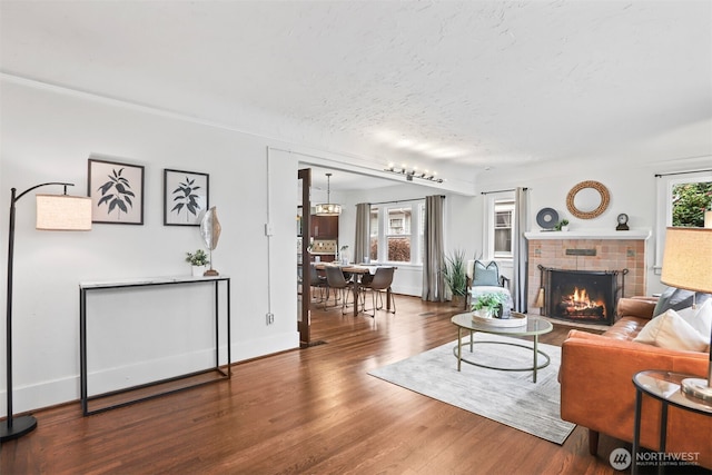 living room with a brick fireplace, a textured ceiling, baseboards, and wood finished floors