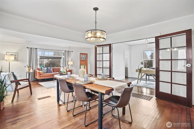 dining space featuring visible vents, crown molding, an inviting chandelier, and wood finished floors