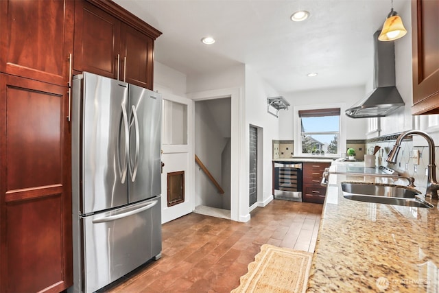 kitchen with wine cooler, freestanding refrigerator, a sink, dark brown cabinets, and wall chimney exhaust hood