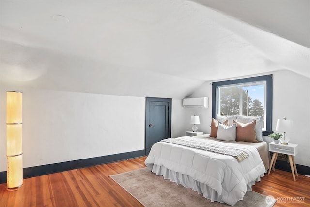 bedroom featuring wood finished floors, baseboards, vaulted ceiling, an AC wall unit, and freestanding refrigerator