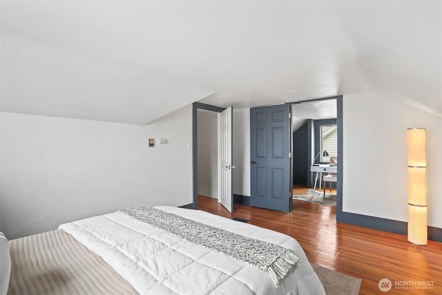 bedroom featuring lofted ceiling, fridge, wood finished floors, and baseboards