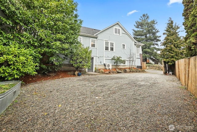 rear view of house with gravel driveway, a garden, and fence