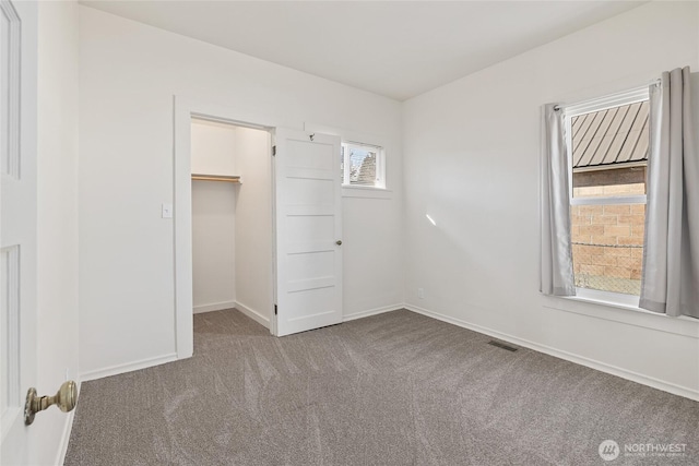 unfurnished bedroom featuring visible vents, baseboards, a walk in closet, carpet floors, and a closet