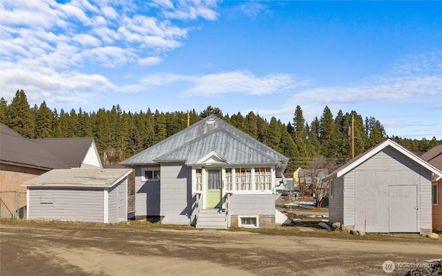 view of front of property featuring entry steps, a storage shed, a forest view, and an outbuilding