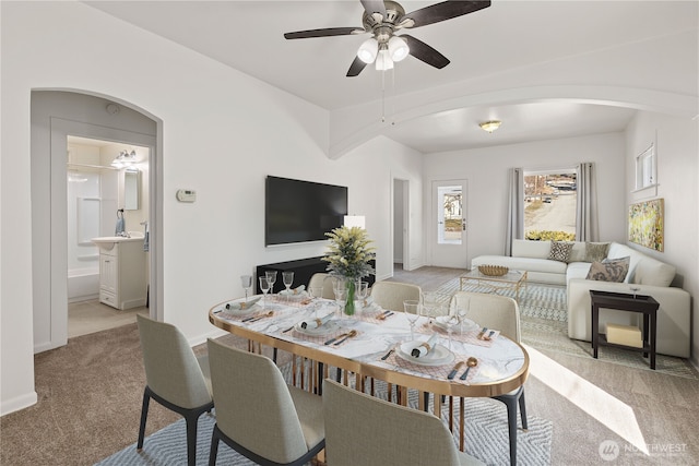 dining area featuring arched walkways, baseboards, a ceiling fan, and light colored carpet