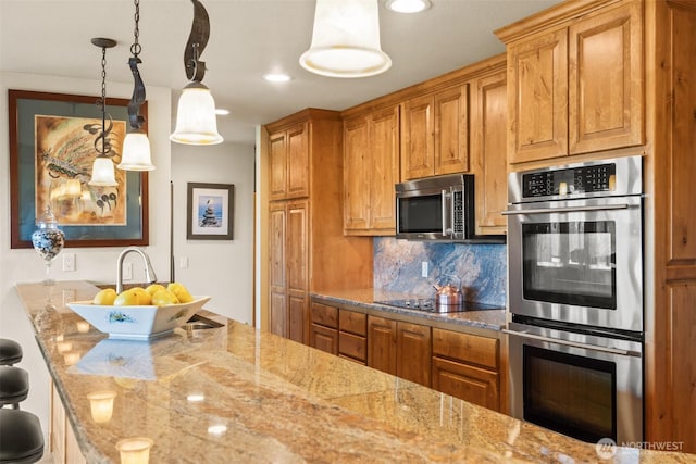 kitchen featuring light stone counters, appliances with stainless steel finishes, brown cabinets, tasteful backsplash, and pendant lighting