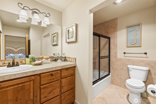 full bathroom with shower / bath combination with glass door, tile walls, toilet, vanity, and tile patterned flooring