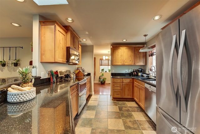 kitchen with a skylight, stainless steel appliances, recessed lighting, a sink, and dark stone countertops