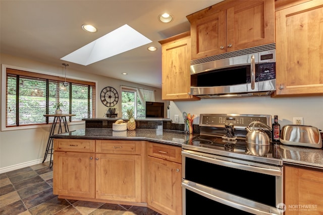 kitchen featuring a skylight, baseboards, appliances with stainless steel finishes, a peninsula, and recessed lighting