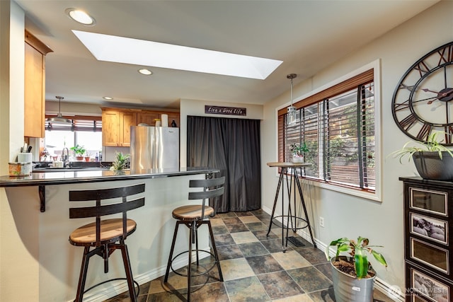 kitchen with a skylight, dark countertops, a kitchen breakfast bar, freestanding refrigerator, and pendant lighting