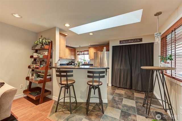 kitchen featuring a skylight, dark countertops, freestanding refrigerator, a peninsula, and hanging light fixtures