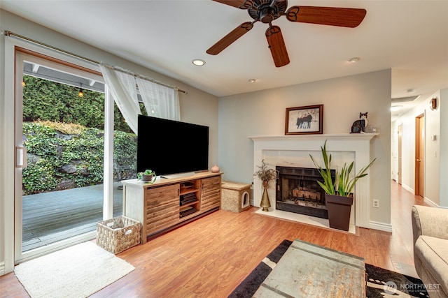 living area featuring ceiling fan, a fireplace, baseboards, and wood finished floors