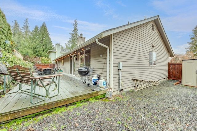 view of property exterior with an outbuilding, a chimney, fence, and a wooden deck