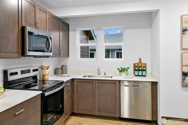 kitchen with appliances with stainless steel finishes, a sink, dark brown cabinetry, and light countertops