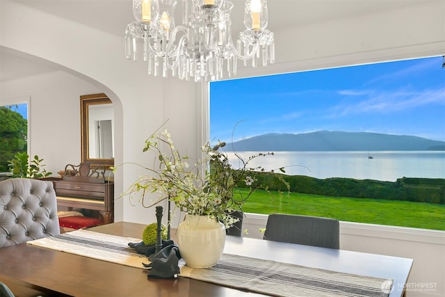 dining space featuring arched walkways, a chandelier, and a water and mountain view