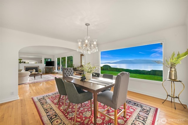 dining area with arched walkways, a notable chandelier, a fireplace, light wood finished floors, and baseboards
