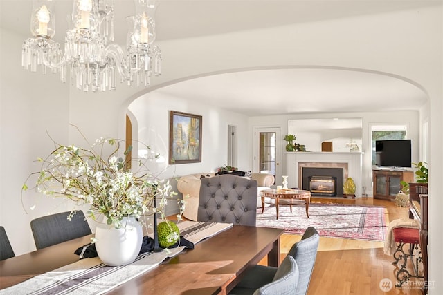 dining space with arched walkways, wood finished floors, and a glass covered fireplace