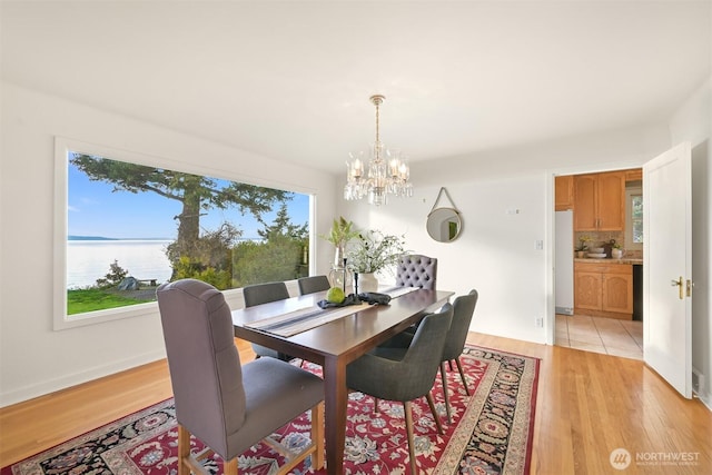 dining room featuring a water view, light wood-style floors, baseboards, and a chandelier