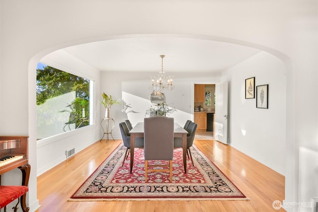 dining space with arched walkways, light wood-style flooring, a chandelier, and visible vents
