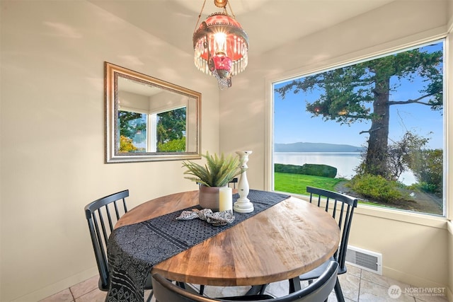 dining area featuring a water view, baseboards, visible vents, and a wealth of natural light