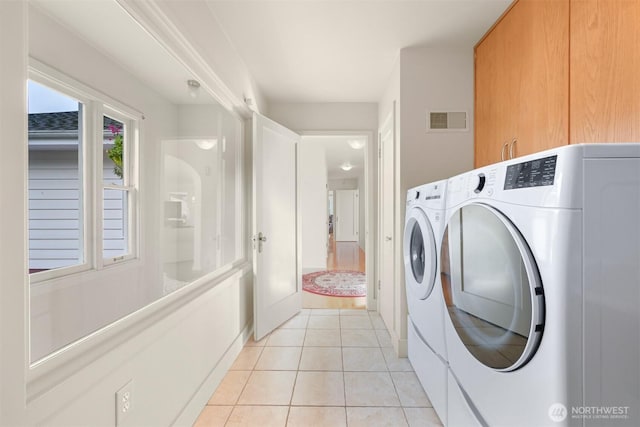 washroom with light tile patterned floors, visible vents, cabinet space, and washing machine and clothes dryer