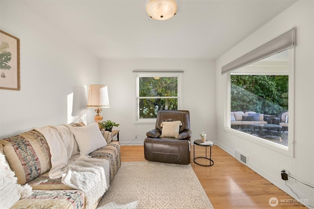 living room featuring baseboards, wood finished floors, visible vents, and a healthy amount of sunlight