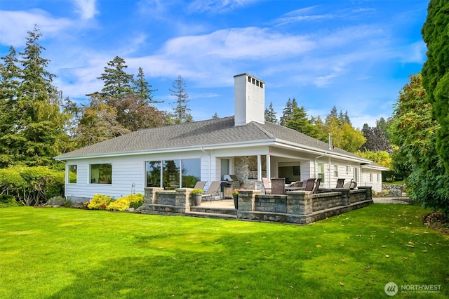 rear view of property featuring a yard, a shingled roof, a chimney, and a patio