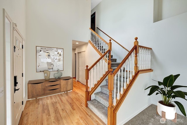 entrance foyer with light wood-type flooring, baseboards, a towering ceiling, and stairway