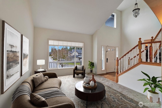 living area featuring baseboards, high vaulted ceiling, wood finished floors, and stairs