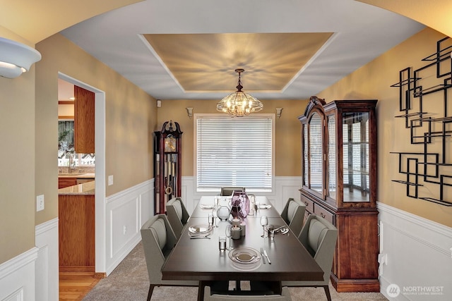 dining space featuring a notable chandelier, a wainscoted wall, arched walkways, and a tray ceiling