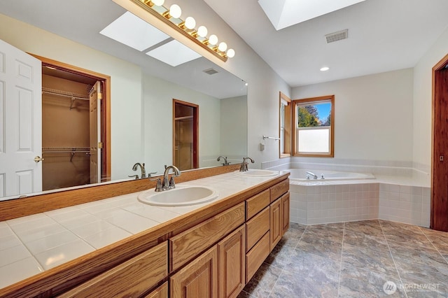 bathroom with a sink, visible vents, a garden tub, and a skylight