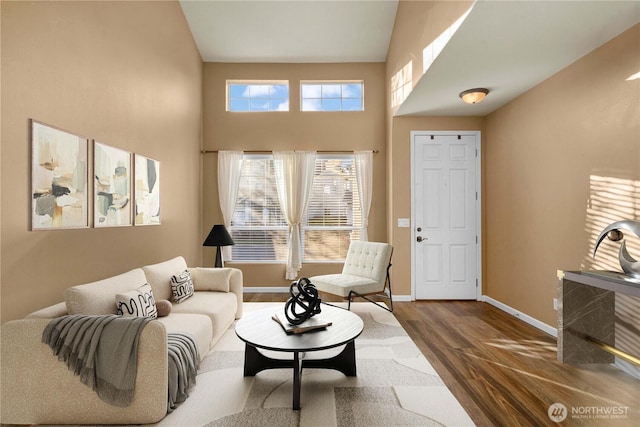 living area featuring a high ceiling, baseboards, and wood finished floors