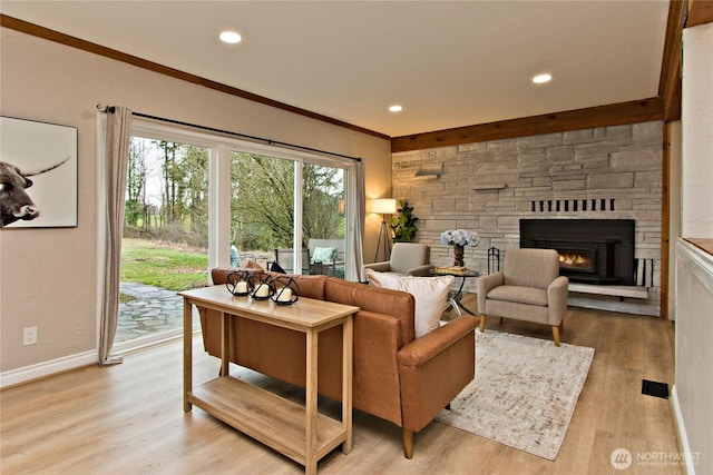 living room featuring light wood finished floors, baseboards, ornamental molding, a stone fireplace, and recessed lighting